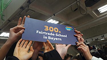 Hände halten das Schild 300. Fairtrade-School in Bayern